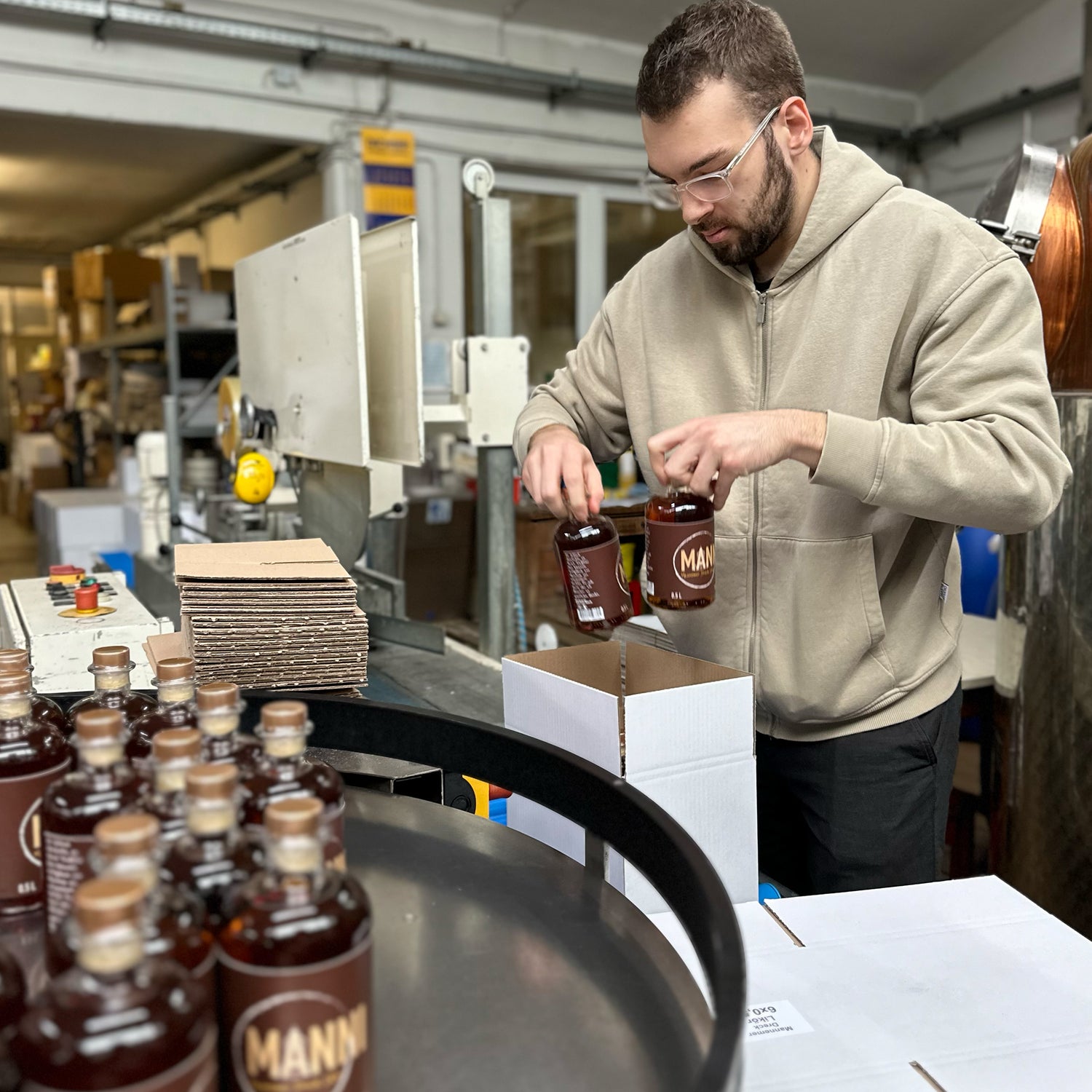 Einer der Gründer packt Getränkeflaschen in Versandkartons, im Hintergrund Lagerregale und Kartons