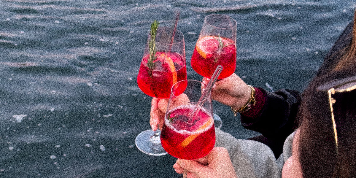 Drei Hände halten Gläser mit GRANADA NIGHTS Spritz, im Hintergrund die glitzernde Wasseroberfläche