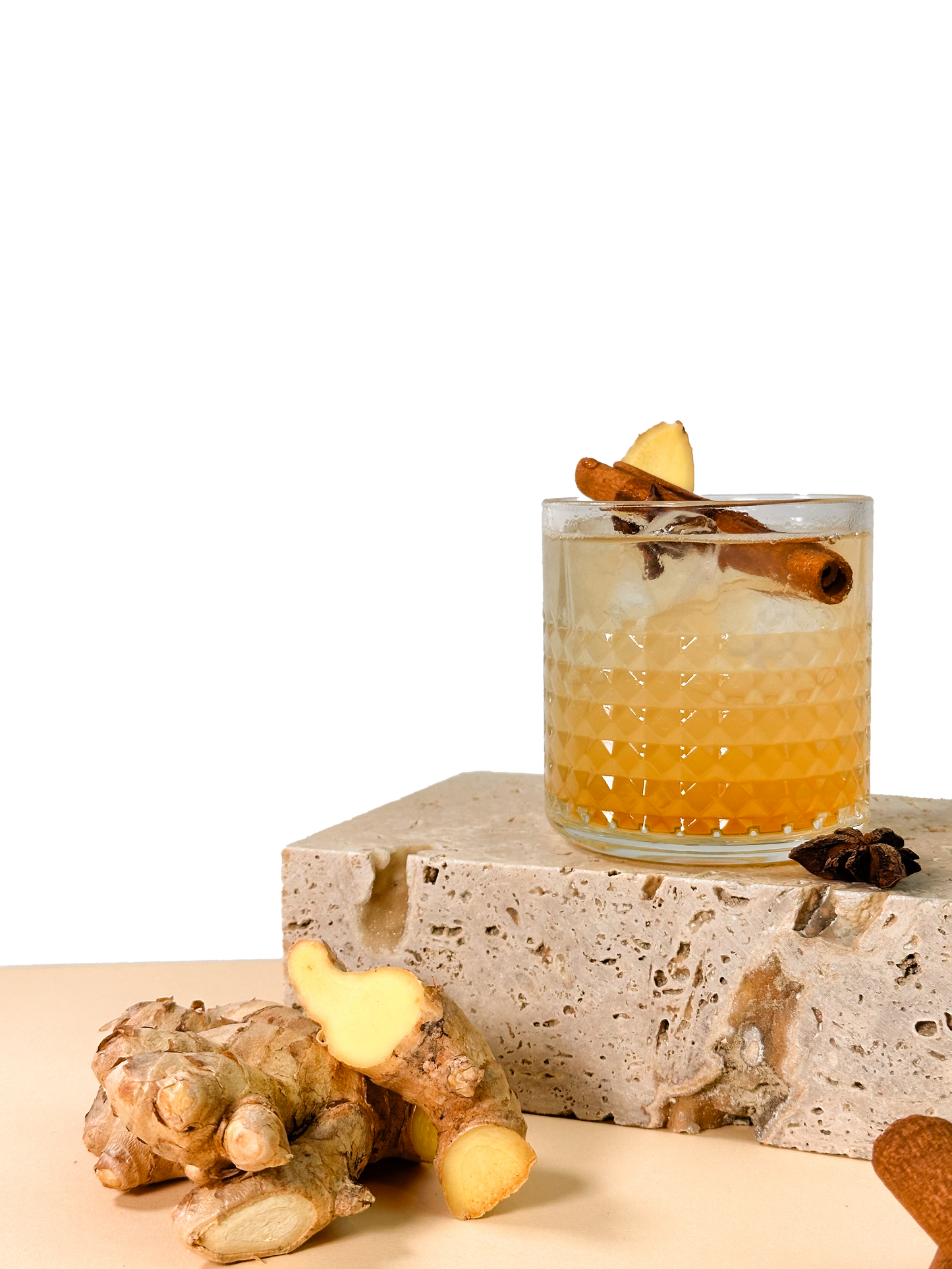 Ein Cocktail mit Ingwerscheibe und Zimtstange in einem Glas auf Stein, daneben eine Ingwerknolle