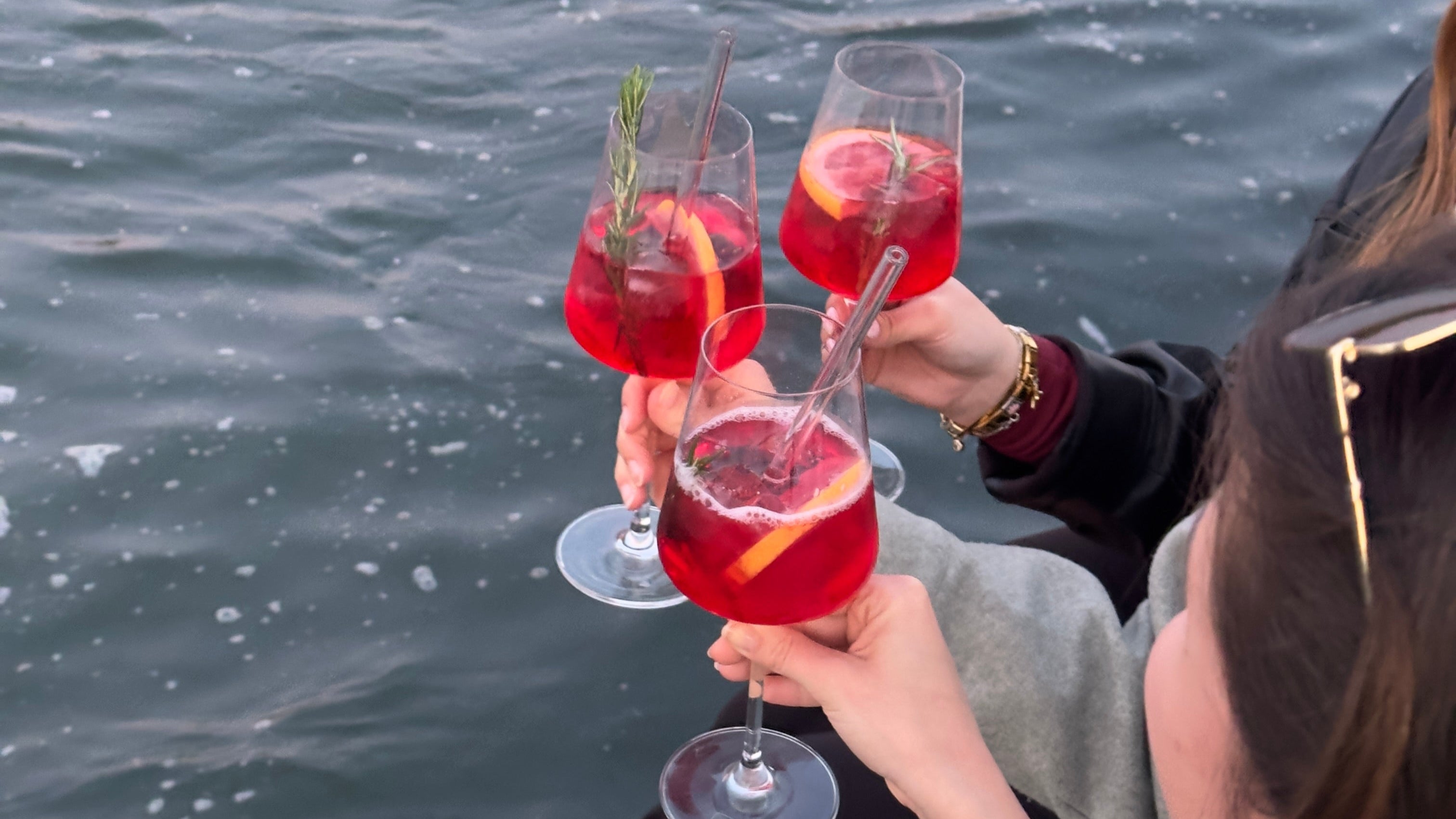 Drei Hände halten Gläser mit GRANADA NIGHTS Spritz, im Hintergrund die glitzernde Wasseroberfläche