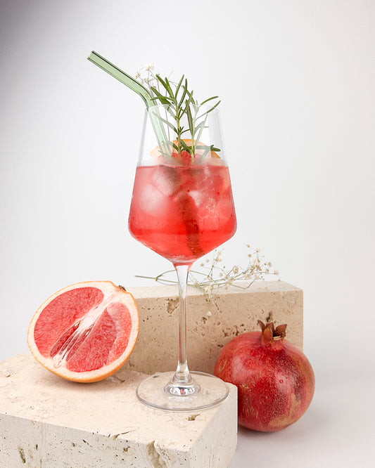 Ein GRANADA NIGHTS Spritz in einem Glas mit Eiswürfeln, Orangenscheibe, Rosmarin und grünem Glasstrohhalm